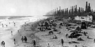 Angelenos play below derricks at Huntington Beach pier, c. 1930-40. In the early decades of the twentieth century, LA residents accepted ground subsidence and small earthquakes as the cost of producing oil. But discontent began to rumble in the late 1930s. Rapid exploitation of Wilmington, one of the largest oil fields in California, and the Huntington Beach field caused Long Beach harbor to sink, buckling railway lines and forcing the city to build higher piers. Credit: Orange County Archives