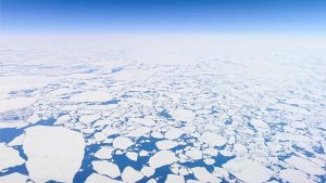 Aerial photo of the endless Arctic ice sheet just off Greenland's west coast, close to the Polar circle. The sheet is broken up in millions of pieces, forming a scattered pattern of white against a dark blue Atlantic ocean and sky. Photo taken from the cockpit of an airliner flying at an altitude of 12 kilometers.