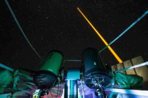 The experiment on La Palma: The laser beam (yellow) generates an artificial guide star in the mesosphere. This light is collected in the receiver telescope (front left). The laser source and the receiver telescope are eight meters away from each other. Credit: Copyright Felipe Pedreros Bustos