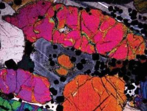 Photomicrograph in crossed polars of precious-metal bearing peridotite. Note the optical zoning (light/dark bands) in the plagioclase (grey coloured mineral) in the central part of the image. The occurrence of this zoning was the focus of the study in question. The width of the image frame is 4 mm. Credit: Nat. Geosci. (2020).