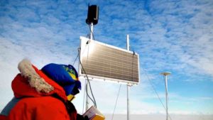 Matthew Siegfried inspects a GPS device, powered by a solar panel at Whillans Ice Plain. Credit: Grace Barcheck/Cornell University