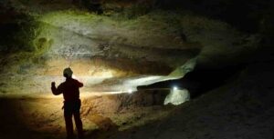 Dimitri Laurent explores a typical gallery in the Nébélé Cave, which was formed by sulfuric acid speleogenesis. You can see a deep notch that indicates the former presence of a river, and sodium sulfate on the left that is produced from weathering by sulfuric acid. Credit: Christophe Durlet