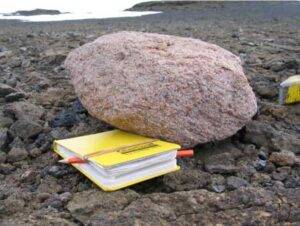 A pink granite boulder next to a yellow notebook for scale. Credit: Jo Johnson, BAS